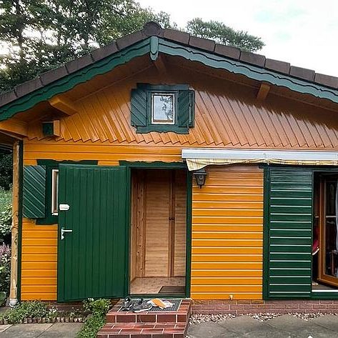 Farbenfrohes Holzhaus mit orangefarbenen Wänden und grünen Fensterläden.